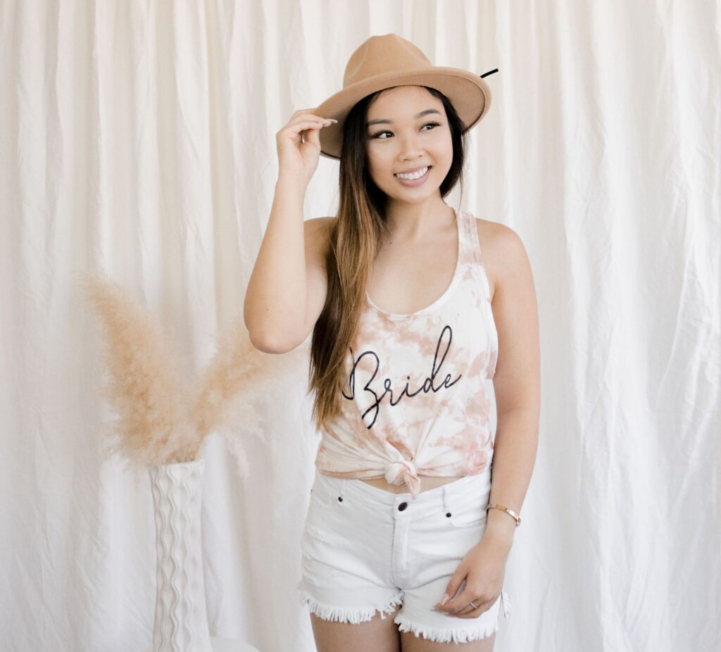 Girl posing in DIY neutral tie dye tank top with "Bride" printed on the front, a tan fedora hat, and white shorts